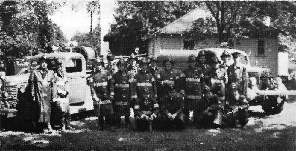 Circa 1945, Pontiac Township firefighters stand grouped together in full gear in front of two fire trucks.